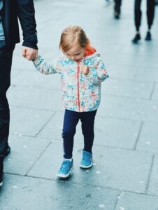 A young girl holds a hand while walking on pavement.