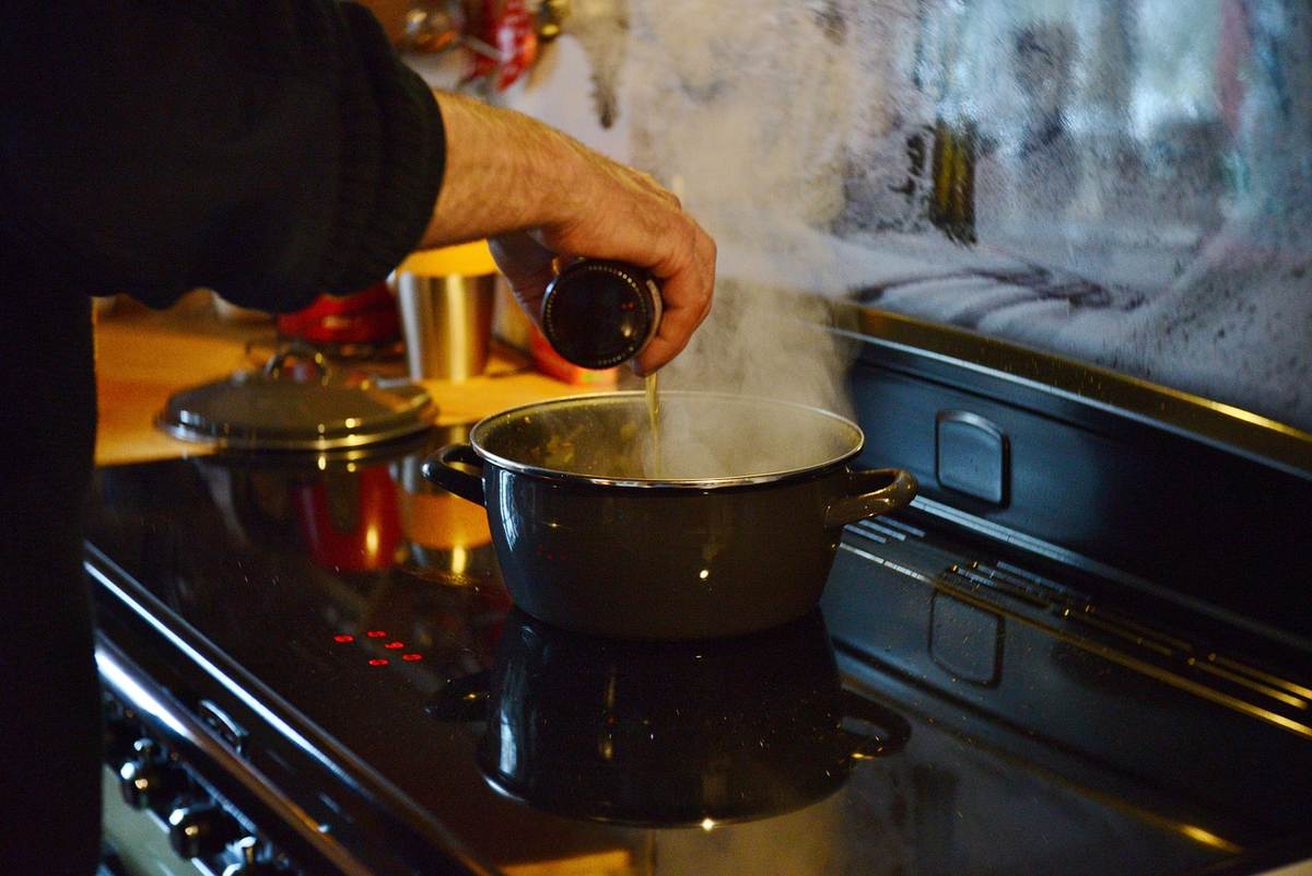 Main versant du liquide dans une casserole fumante sur une cuisinière
