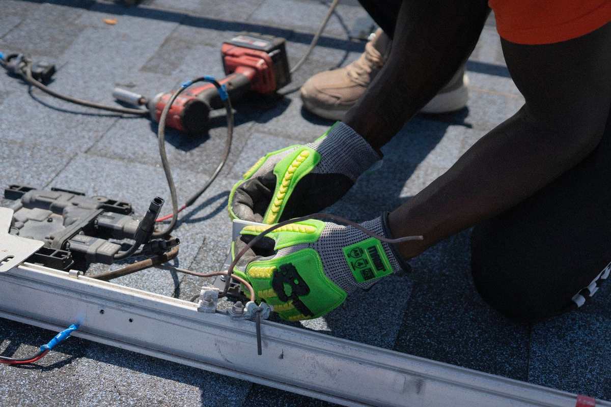 Main d'ouvrier noir portant gants jaunes manipulant fil électrique sur une structure métallique extérieure