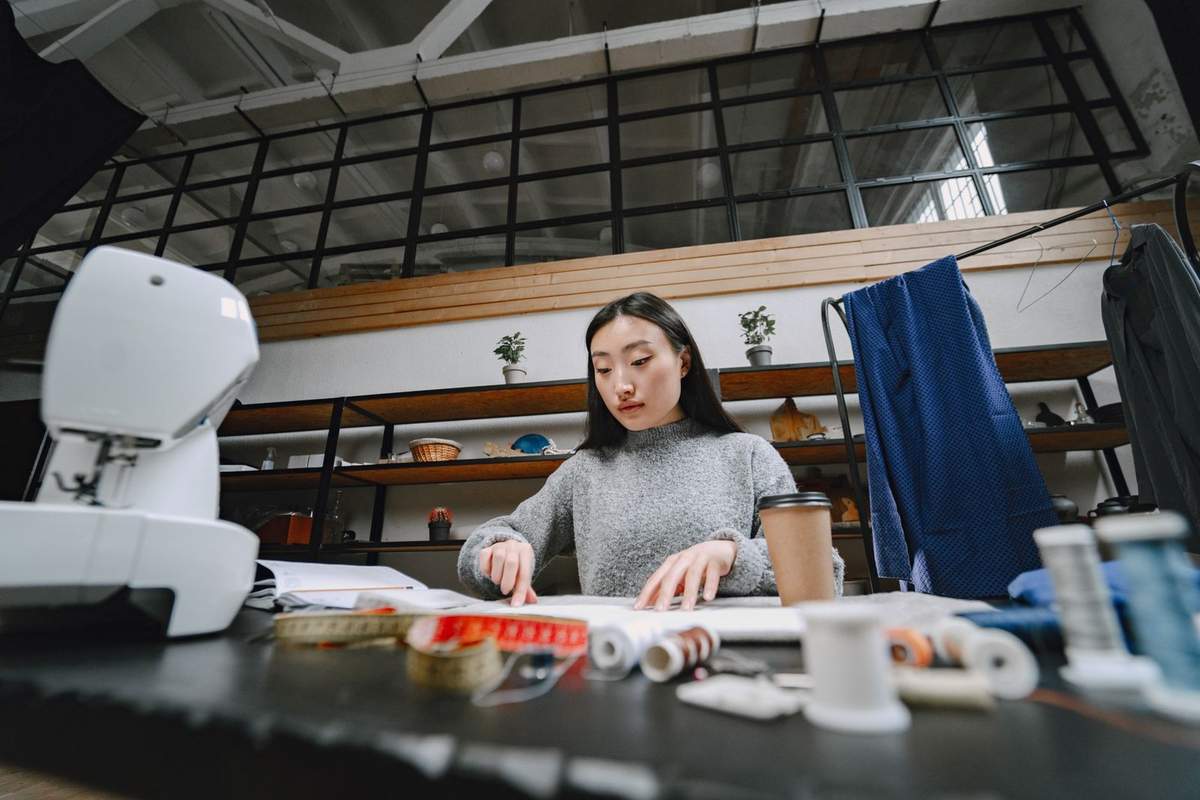 Femme utilisant une machine à coudre avec des fils et du tissu sur une table dans un atelier