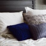 Un lit avec plusieurs oreillers et couvertures, tête de lit sombre, lampe