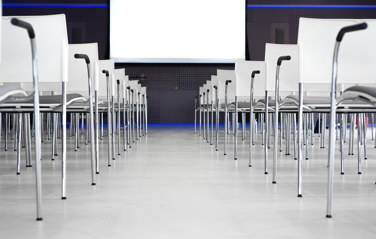 Rangées de chaises blanches face à un écran blanc dans une salle