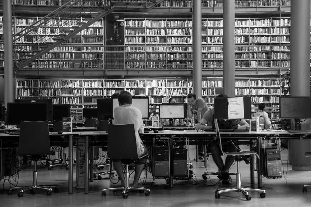 Salle de lecture d'une bibliothèque universitaire avec des étudiants travaillant sur des ressources numériques Salle de lecture d'une bibliothèque universitaire avec des étudiants travaillant sur des ressources numériques