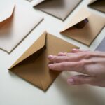 Une main pose doucement une enveloppe marron sur une surface claire