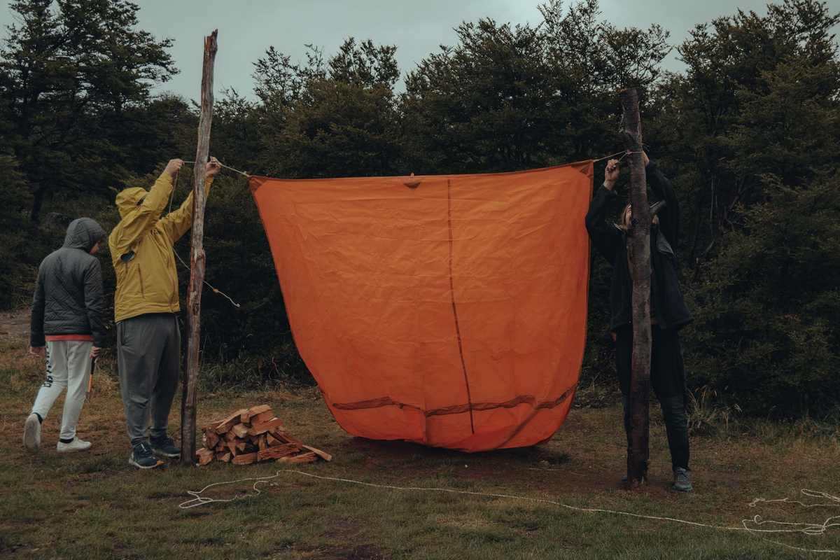 Trois personnes accrochent une grande toile orange entre deux poteaux Trois personnes accrochent une grande toile orange entre deux poteaux